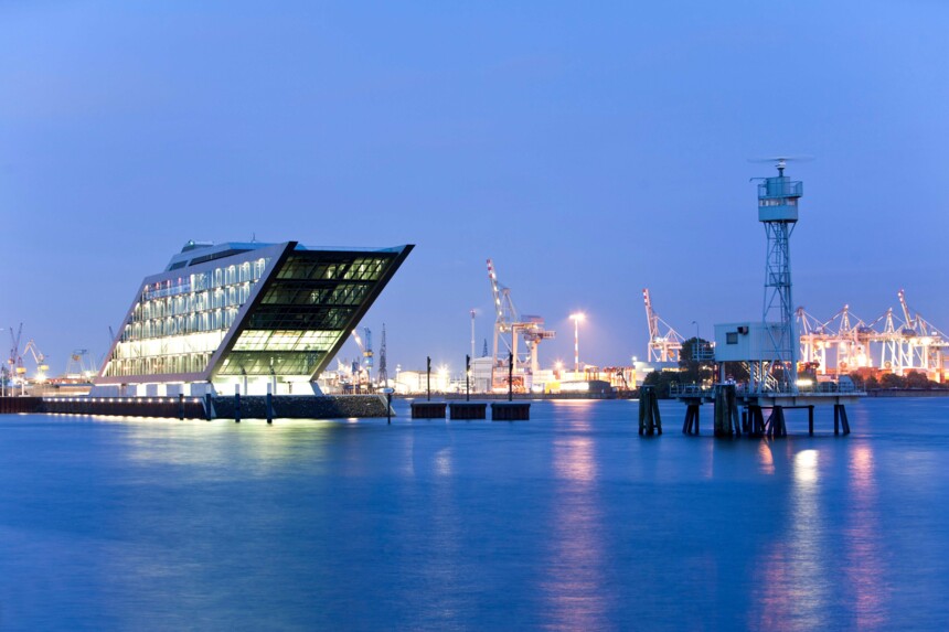 Beleuchtetes Dockland-Gebäude und Hafenkräne bei Abenddämmerung am Hamburger Hafen.