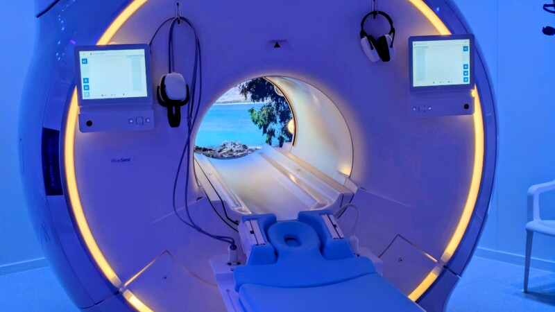 Moderne MRT-Maschine mit blauem Licht und Blick auf Meer und Bäume durch den Tunnel.